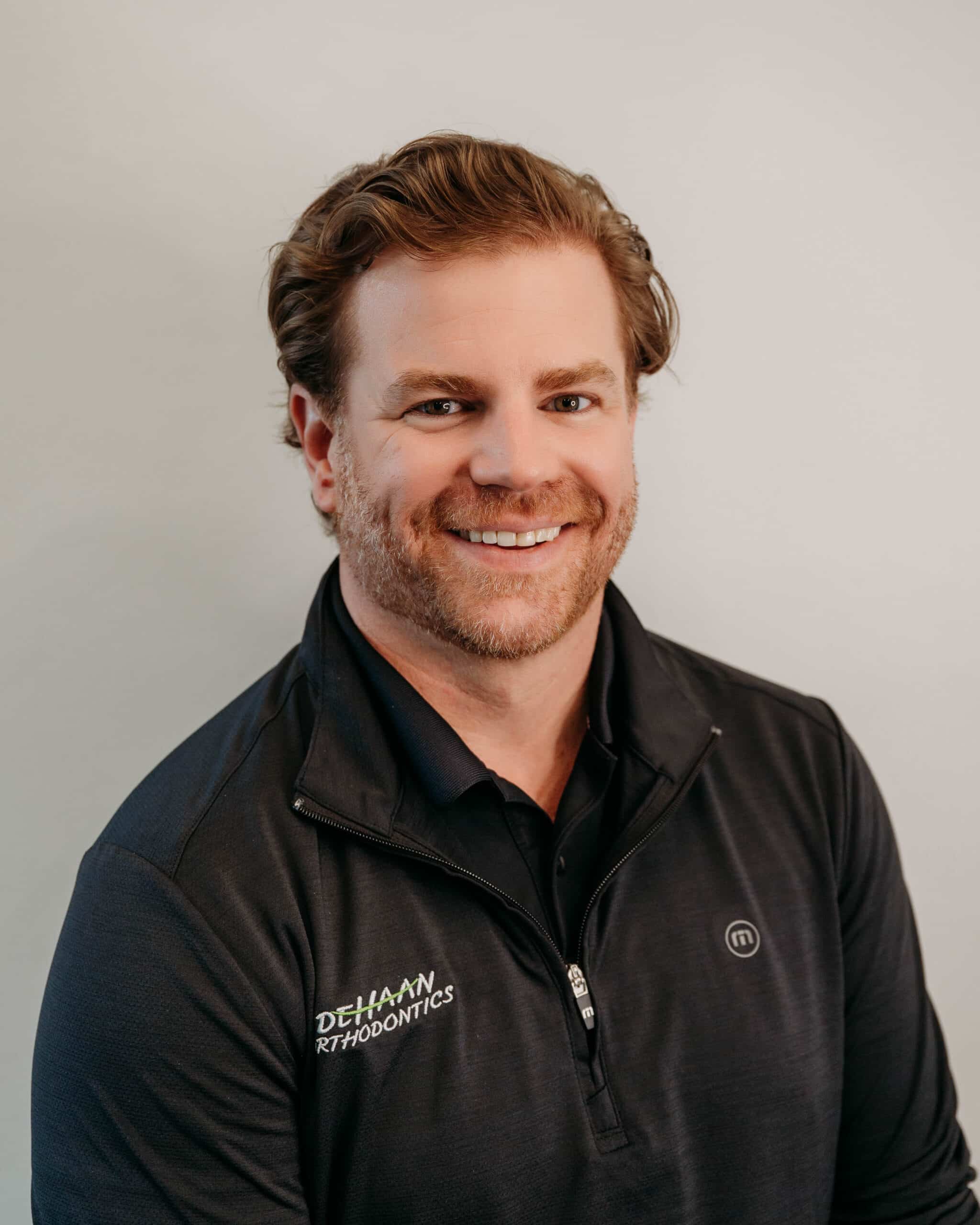 Dr. Andrew DeHaan smiling confidently in a branded jacket, orthodontist and founder of DeHaan Orthodontics in Lake Orion, MI