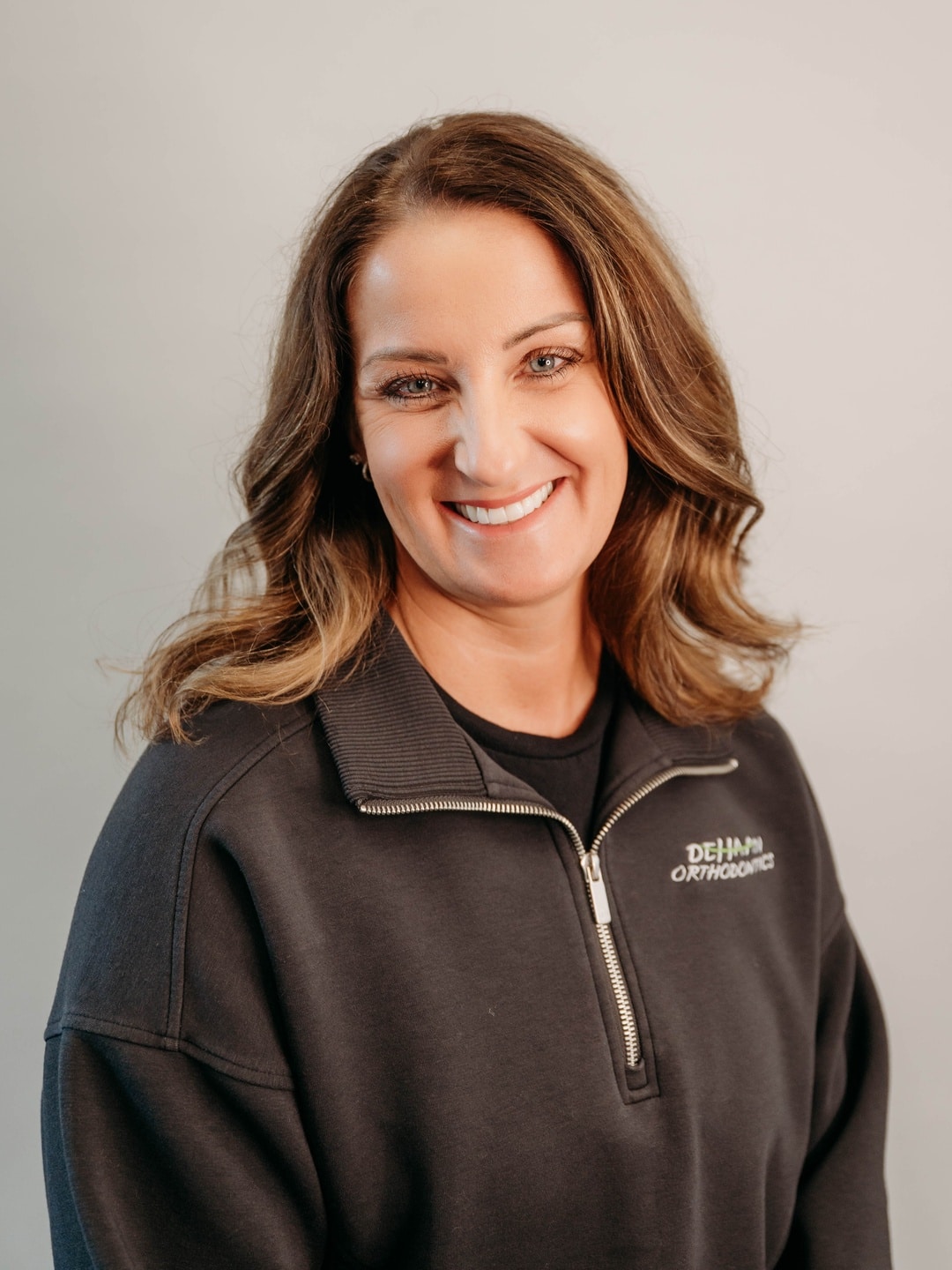 Jen, Office Manager at DeHaan Orthodontics, smiling in a branded team jacket at DeHaan Orthodontics in Lake Orion, MI