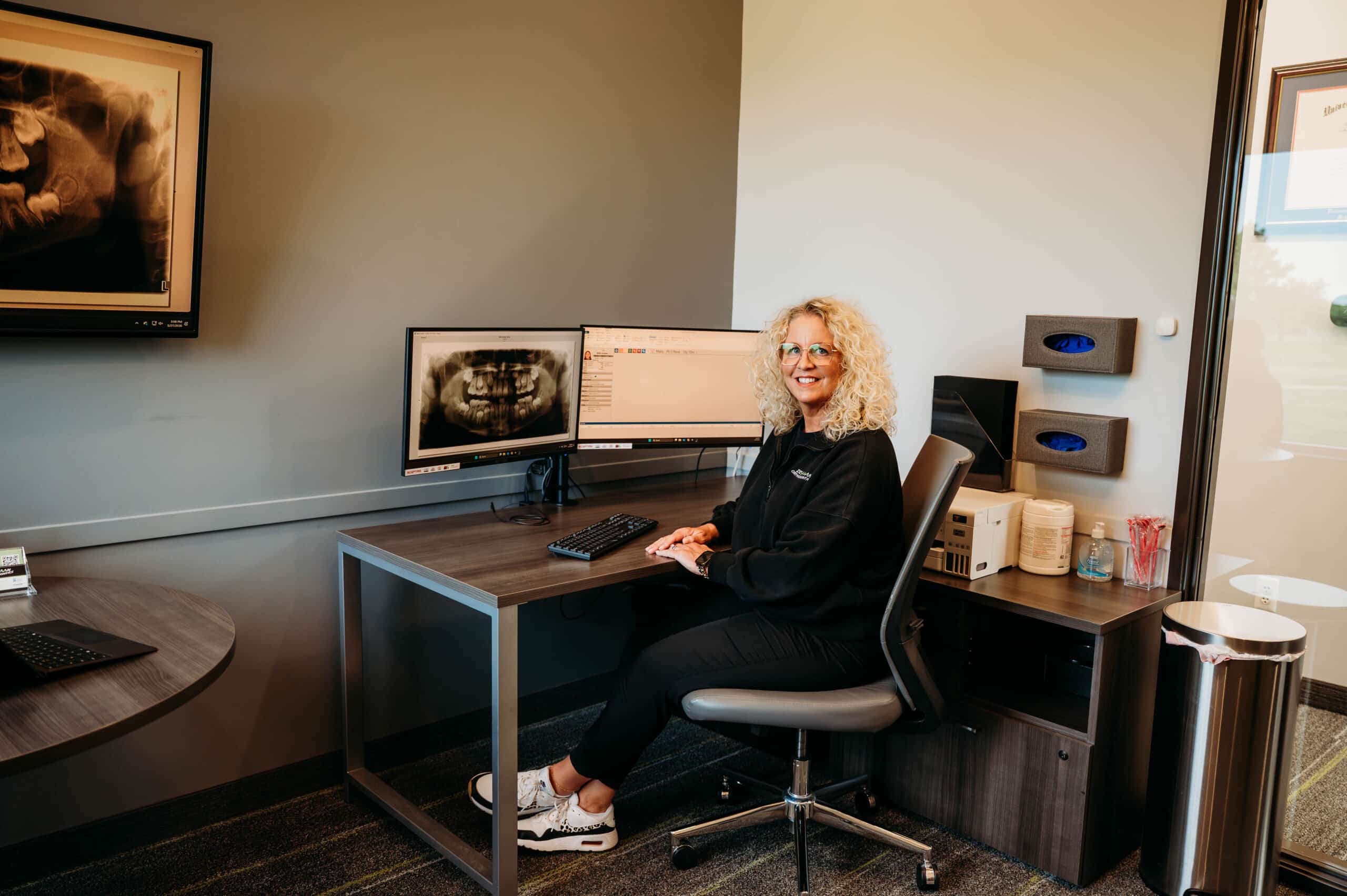 Team member seated at a desk with dental imaging screens in the consultation area at DeHaan Orthodontics in Lake Orion, MI