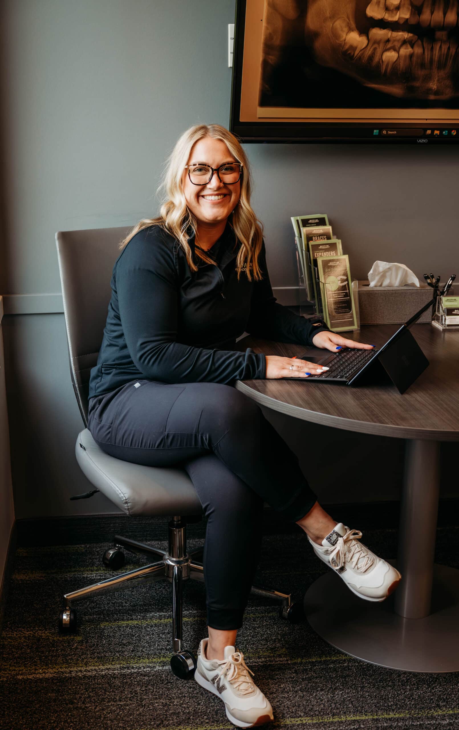 Team member seated at a consultation table with a laptop in the patient consultation area at DeHaan Orthodontics in Lake Orion, MI