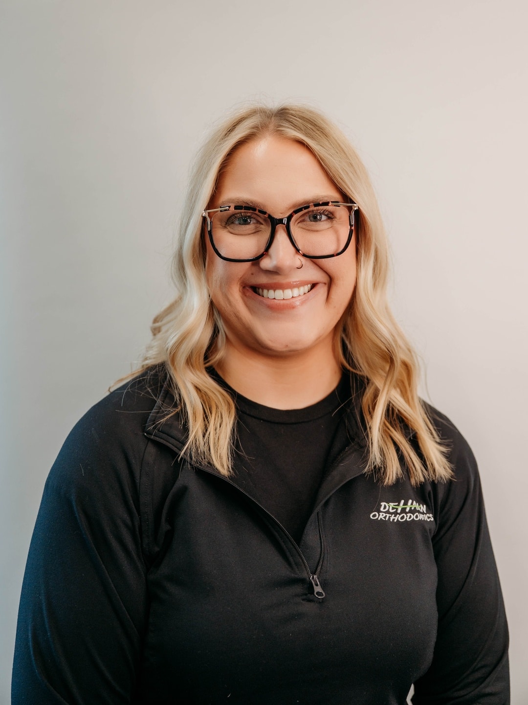 Kailey, Treatment Coordinator at DeHaan Orthodontics, smiling in a branded team jacket at DeHaan Orthodontics in Lake Orion, MI