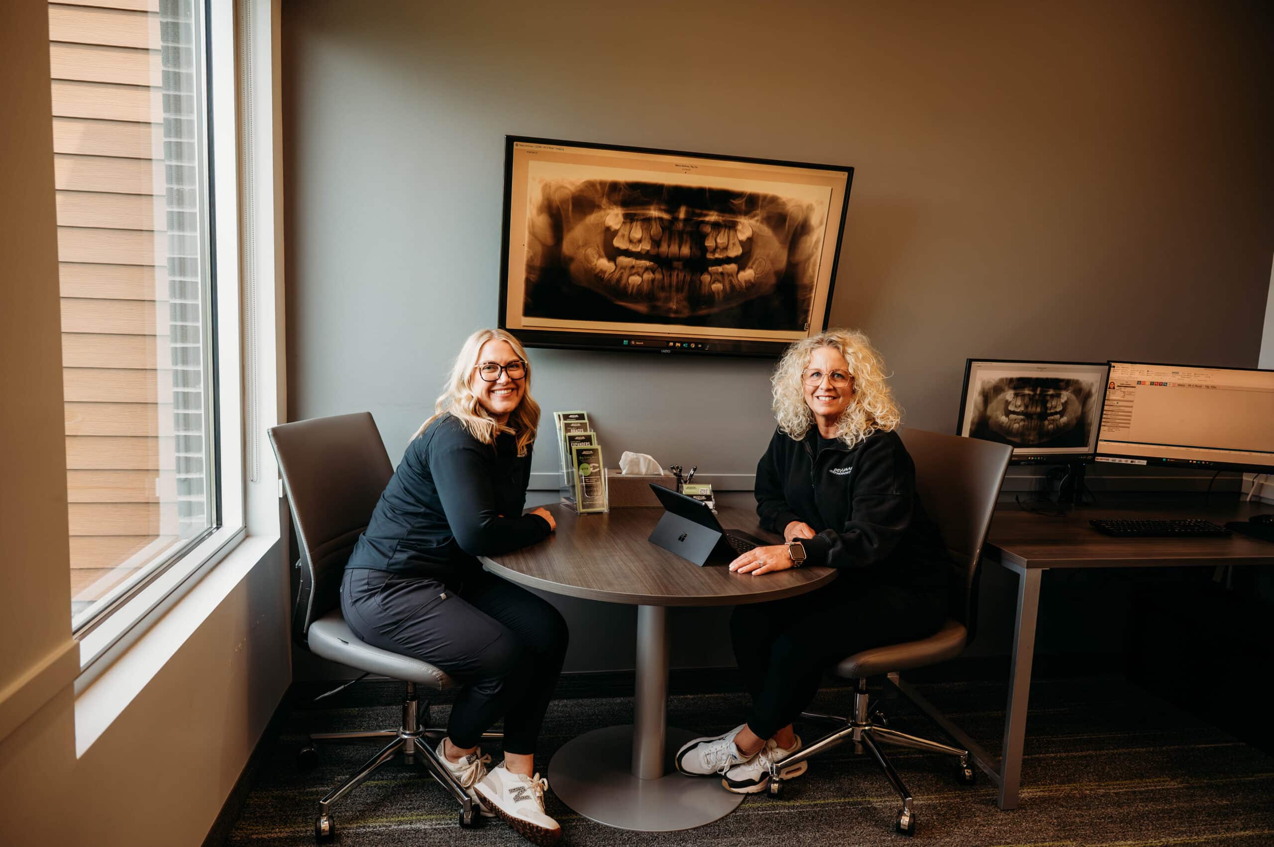 Two team members seated at a consultation table near a window in the patient consultation area at DeHaan Orthodontics in Lake Orion, MI