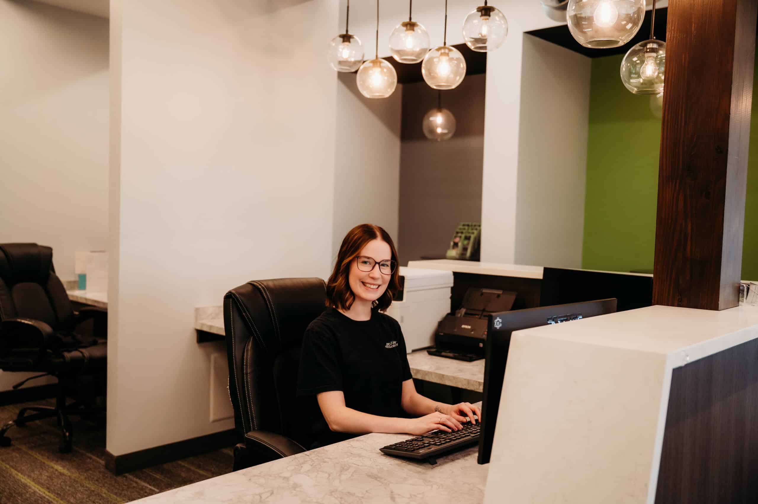 Front desk team member working at the reception desk under modern pendant lighting at DeHaan Orthodontics in Lake Orion, MI