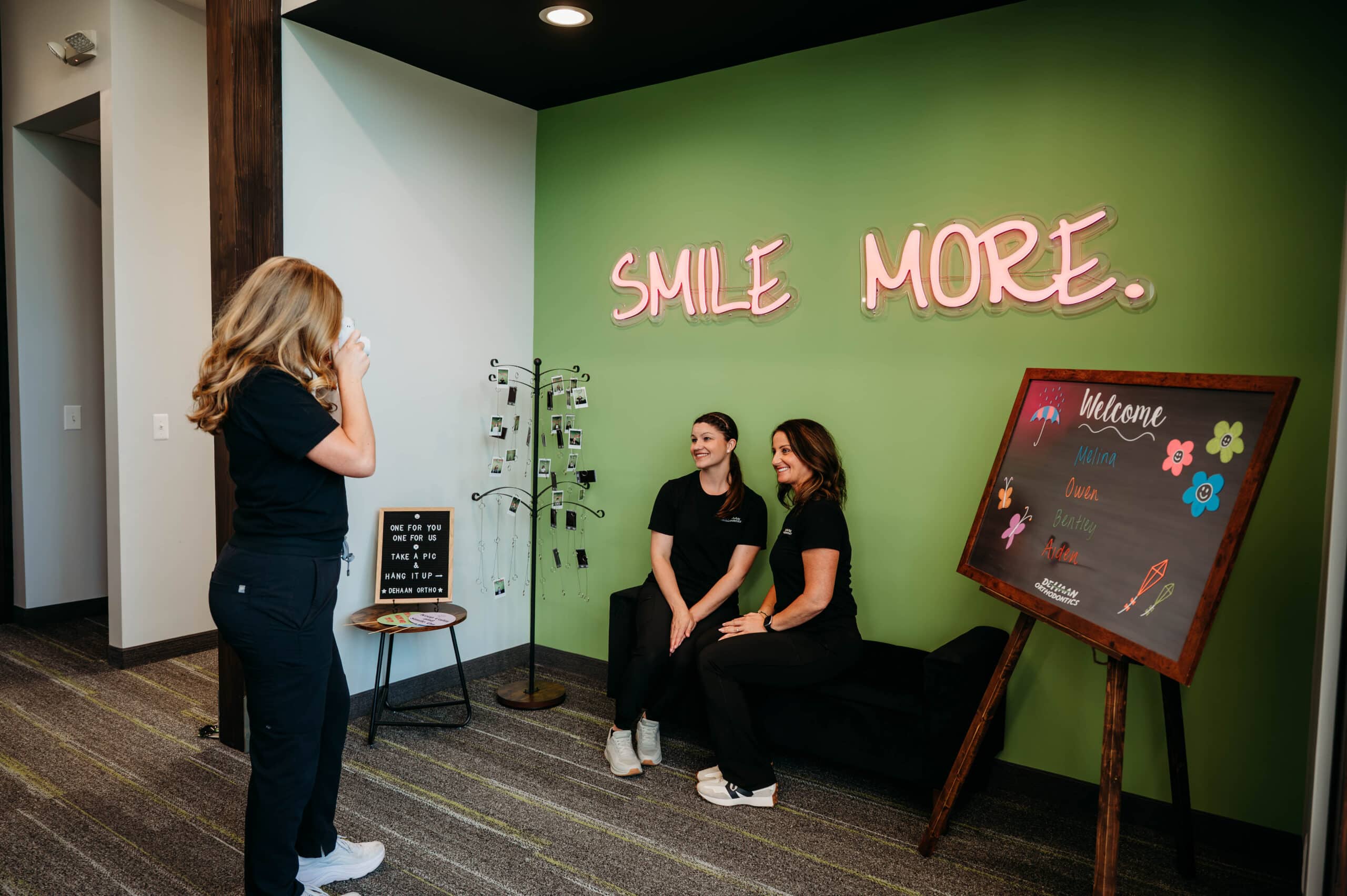 Two team members relaxing in the waiting area in front of the Smile More wall sign at DeHaan Orthodontics in Lake Orion, MI
