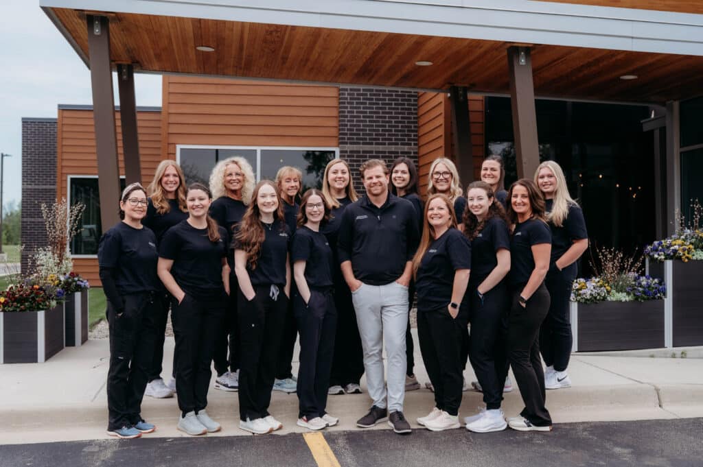 Dr. DeHaan and the full team posing together in front of the DeHaan Orthodontics office building at DeHaan Orthodontics in Lake Orion, MI