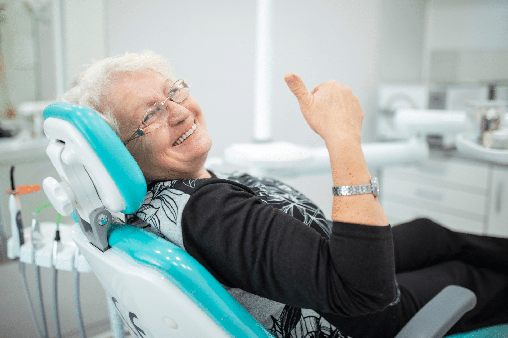 Older woman smiling and giving a thumbs-up while seated in a dental chair