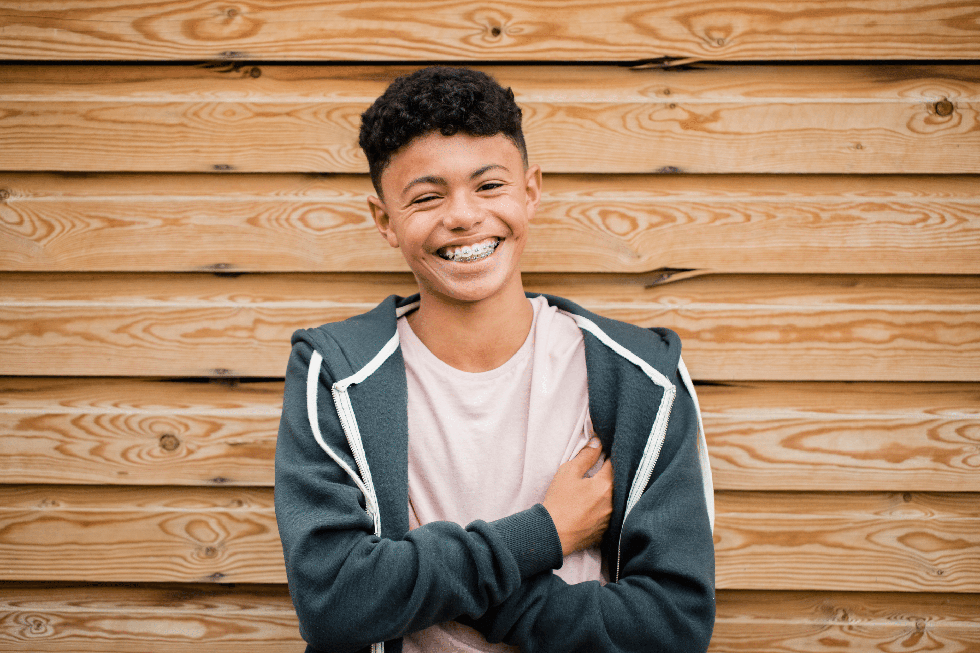 Smiling teen wearing metal braces in front of a wooden wall